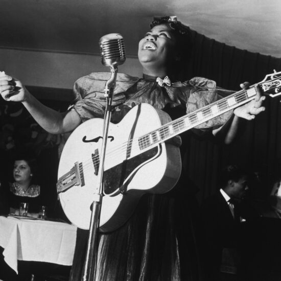 American gospel singer Sister Rosetta Tharpe standing onstage, singing at the microphone with her guitar, at Cafe Society Downtown, New York City, December 11, 1940
