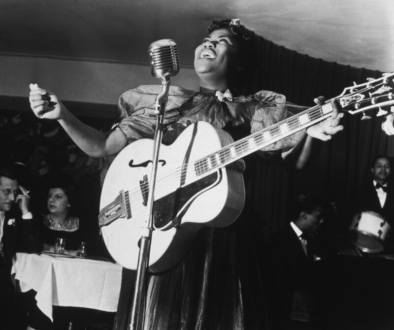 American gospel singer Sister Rosetta Tharpe standing onstage, singing at the microphone with her guitar, at Cafe Society Downtown, New York City, December 11, 1940