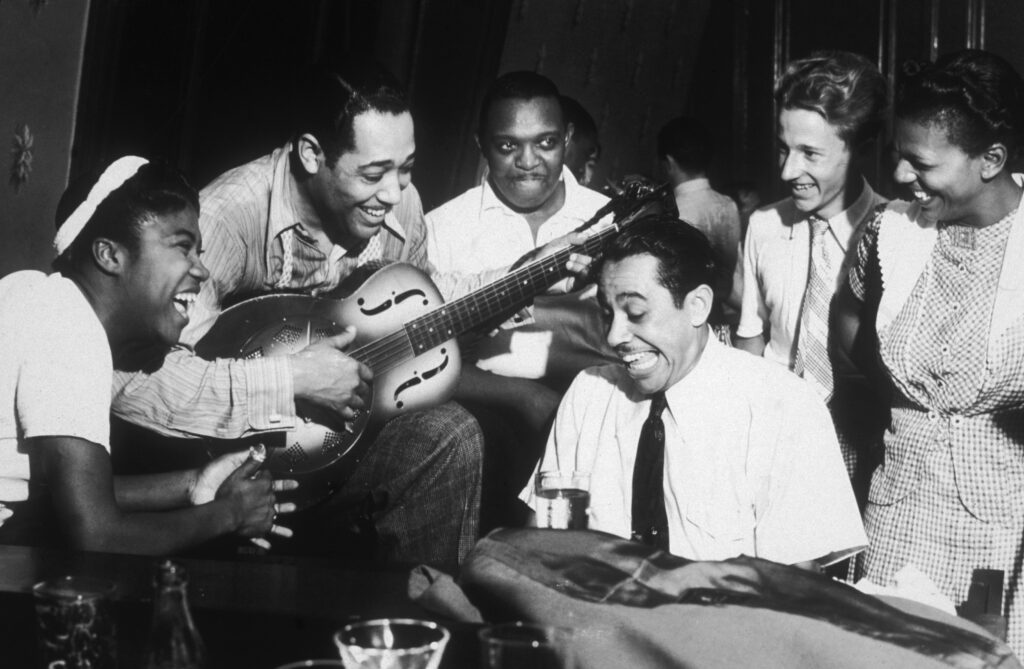 August 1939: American composer and bandleader Duke Ellington (1899 - 1974) plays guitar and Cab Calloway (1907 - 1994) plays piano during a jam session at a private party hosted by Hearst political cartoonist Burris Jenkins, in his studio, New York City. Sister Rosetta Tharpe attends.