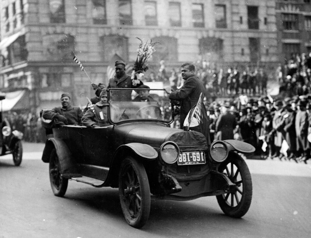 Croix de guerre medal winner Private William Henry Johnson (1892 - 1929) holds a bouquet of flowers and stands in an open top automobile during the victory parade in New York, February 17, 1919. He was a member of the 369th Infantry Regiment (the Harlem Hellfighters).