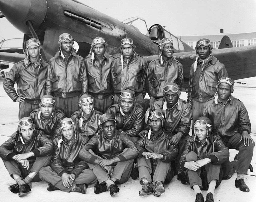 Photograph of Class SE 43 K newly commissioned pilots (Tuskegee Airmen) at Tuskegee Army Flying School, in bomber jackets with a fighter airplane, Tuskegee, Alabama, 1942.