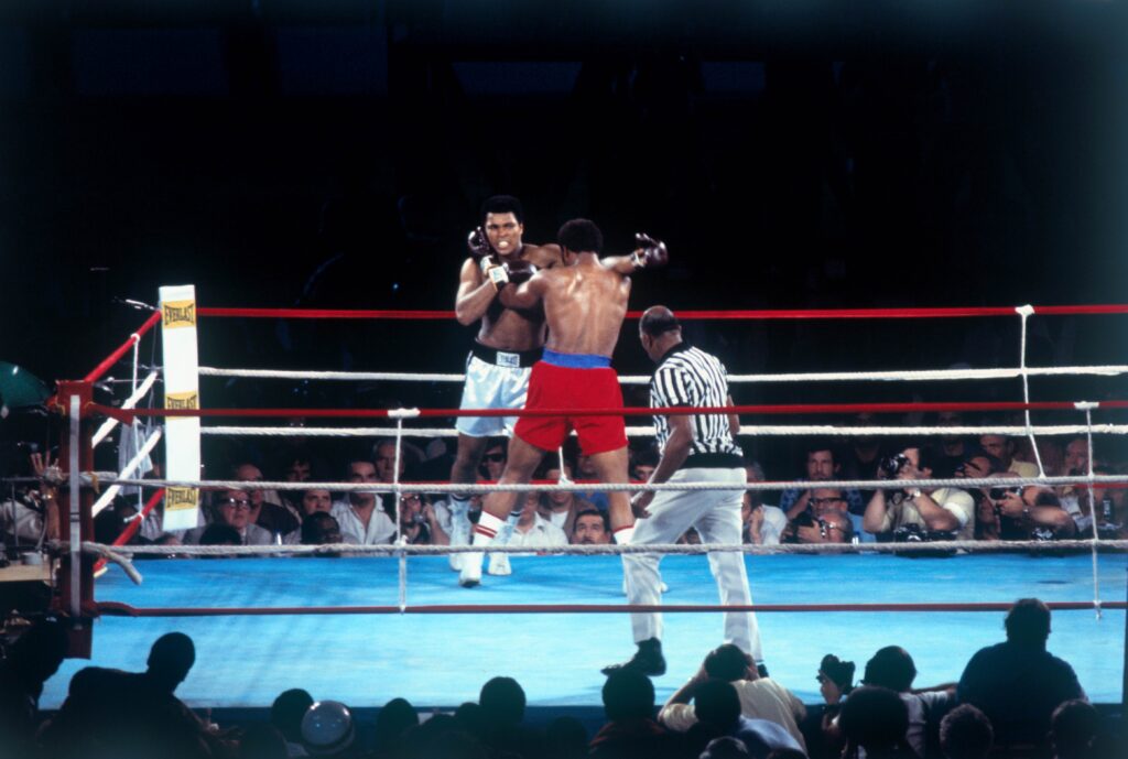 Muhammad Ali throws a hard right to the head of George Foreman in 1st round action in the world heavyweight title bout, Kinshasa, Zaire, 10/30/1974. Ali defeated Foreman in the 8th round by a knockout to regain the crown. Slide shows Foreman (red trunks) putting his fist over Ali's shoulder.