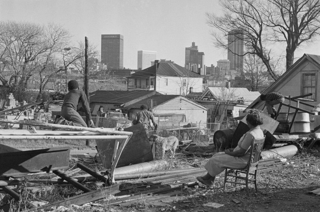 12/23/71 Atlanta: A young mother watches her children play in the trash which litters the downtown slum areas and is overshadowed by the modern skyscrapers that make up the Atlanta skyline.