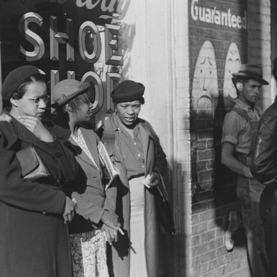 A photograph of three African American women who were identified as domestic helpers waiting for a street car, all three women are wearing coats and hats, two men and a woman who are white are also waiting on transportation, Atlanta, Georgia. 1939. From the New York Public Library.