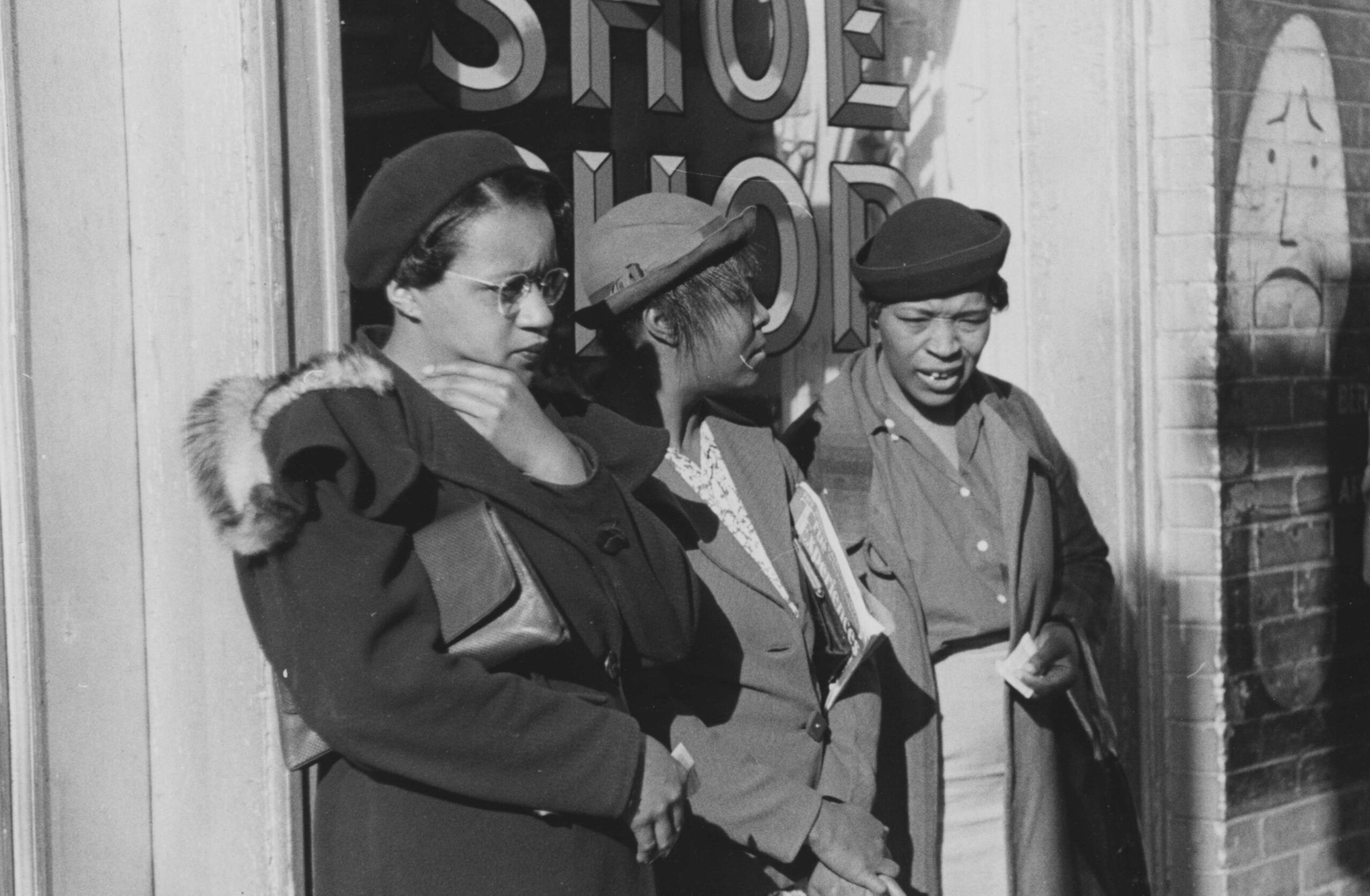 A photograph of three African American women who were identified as domestic helpers waiting for a street car, all three women are wearing coats and hats, two men and a woman who are white are also waiting on transportation, Atlanta, Georgia. 1939. From the New York Public Library.