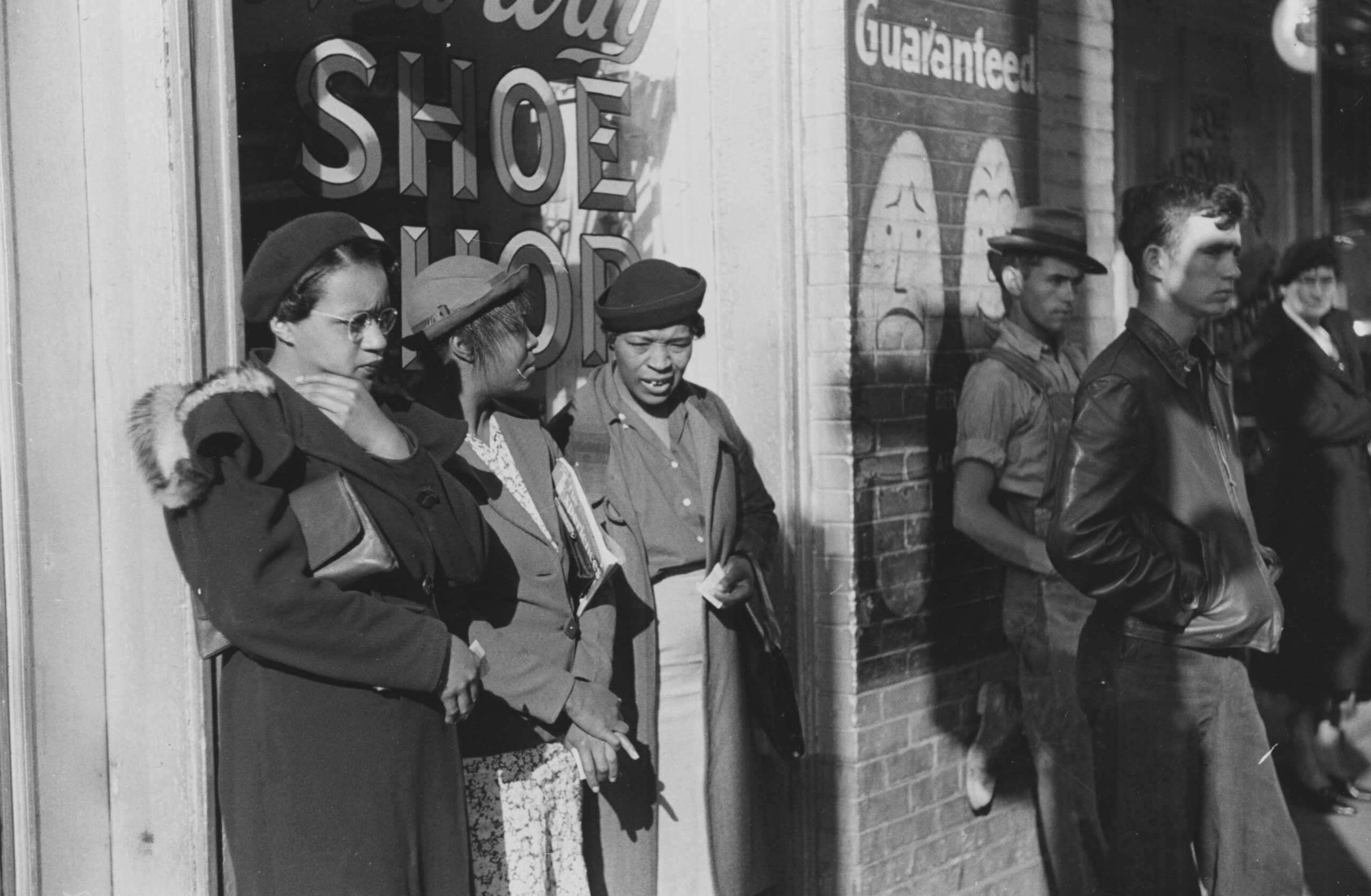 A photograph of three African American women who were identified as domestic helpers waiting for a street car, all three women are wearing coats and hats, two men and a woman who are white are also waiting on transportation, Atlanta, Georgia. 1939. From the New York Public Library.