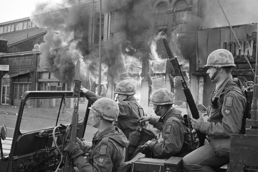 4/6/1968-Washington, DC: Flames pour from a building in the background as troops in a Jeep patrol Seventh Street April 6 as looting and arson continues in the nation's capital. Five persons have been killed here since violence erupted after the slaying of Dr. Martin Luther King Jr. Photograph by UPI staff photographer Darryl Heikes.